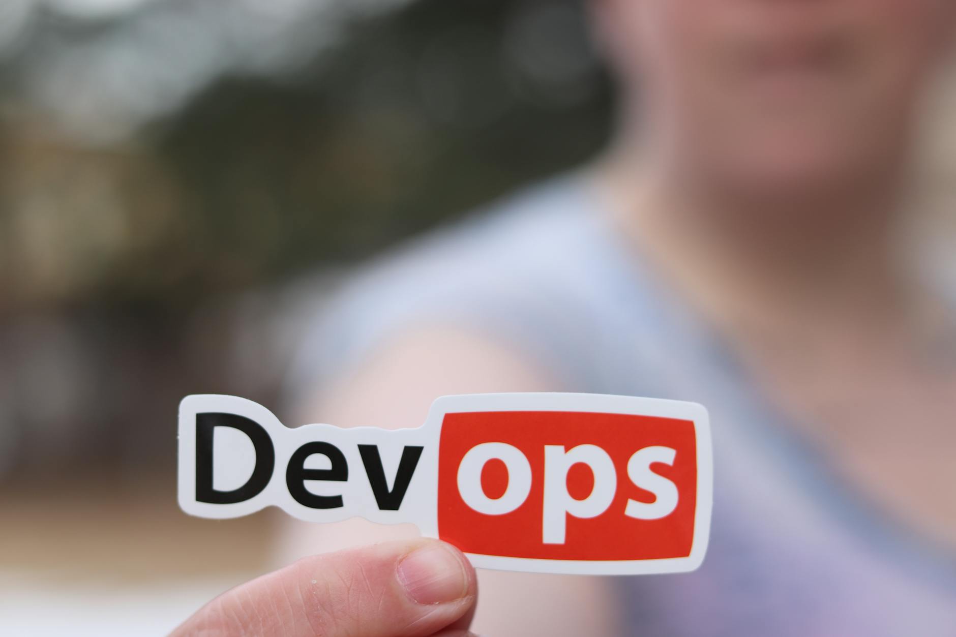 Osoba trzyma naklejkę DevOps w otwartej przestrzeni outdoors
