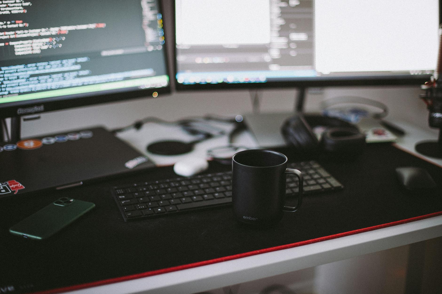 Domowe biuro programisty z dwoma monitorami, klawiaturą i czarnym kubkiem