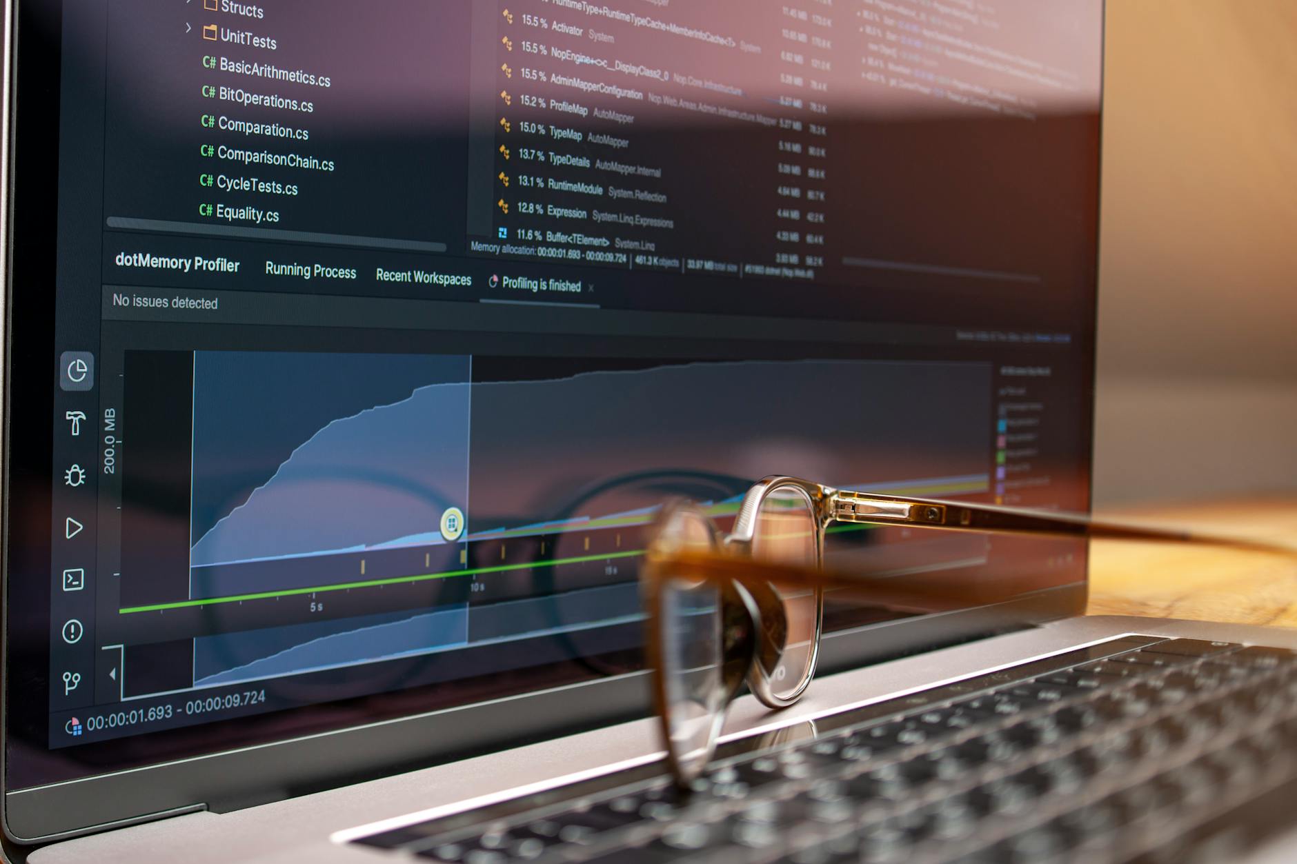 Laptop z kodem i wykresami wydajności, okulary leżą na klawiaturze