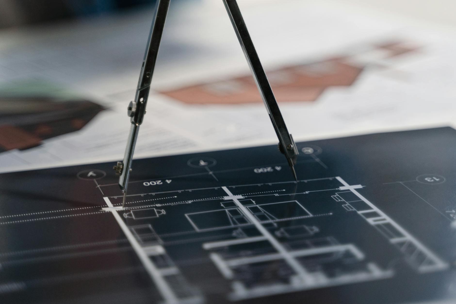 Cyrkiel leżący na planach architektonicznych symbolizujących planowanie systemu