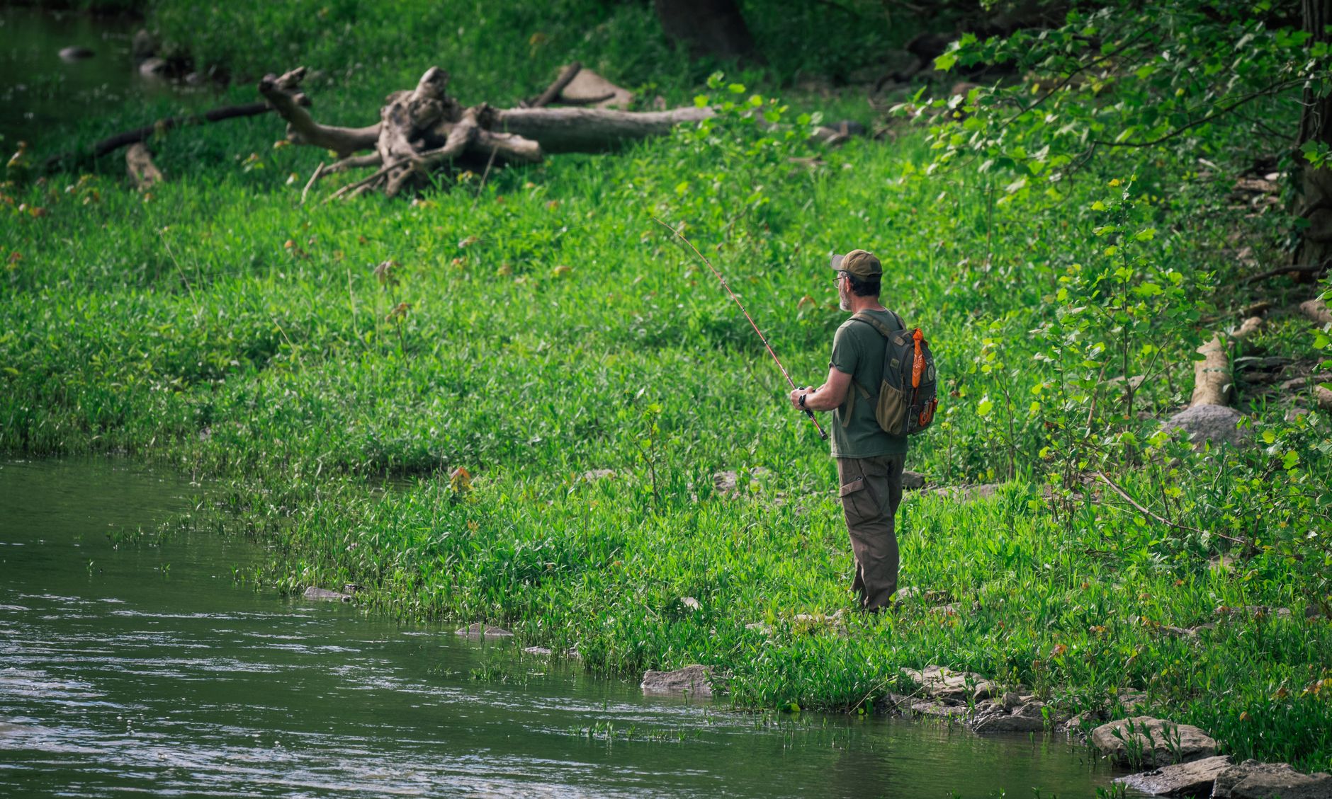 Wędkarz nad dużą rzeką wśród zieleni podczas spokojnego łowienia